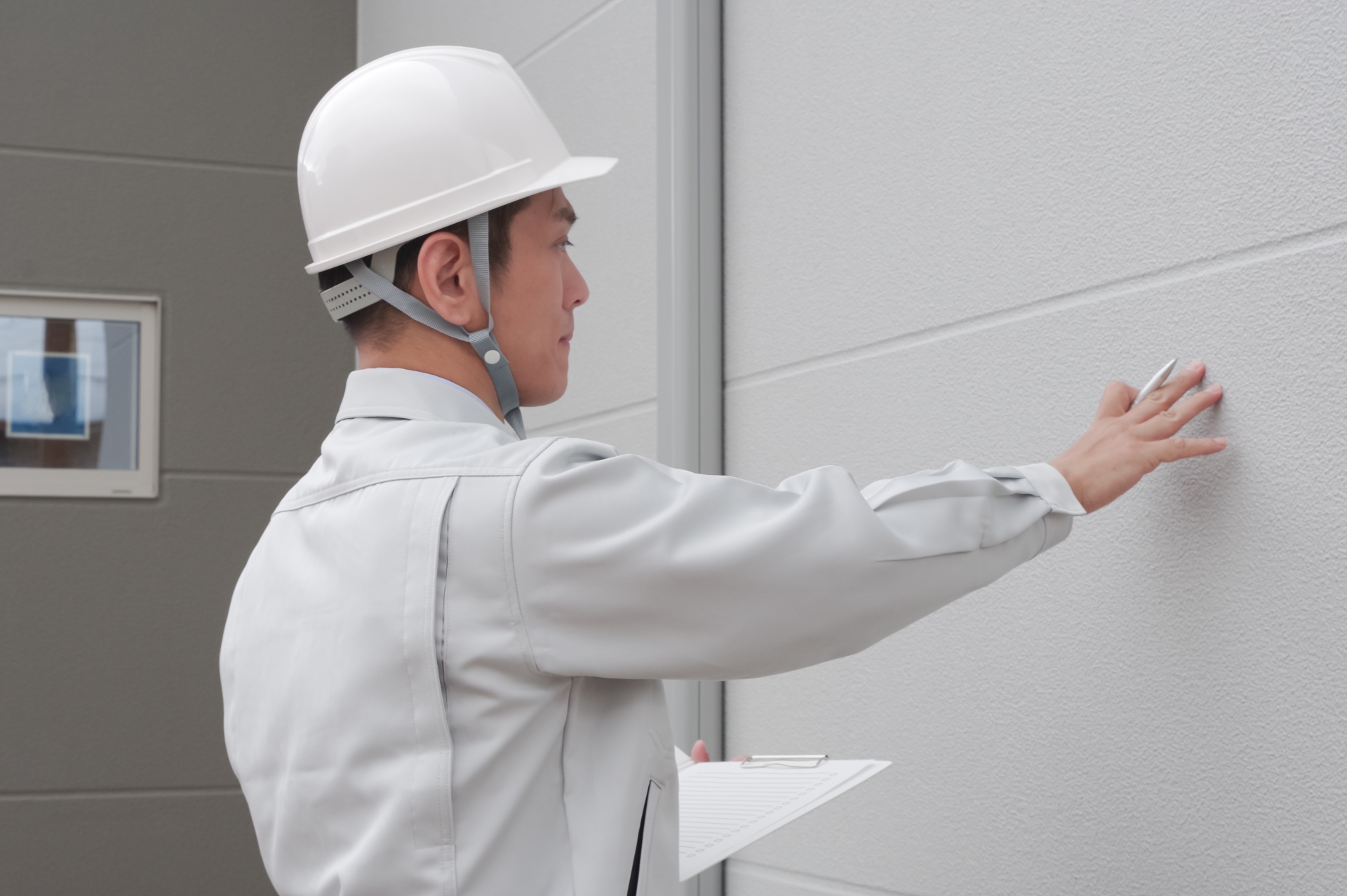 ヘルメットを着用した作業員が建物の外壁の状態を手で確認している様子